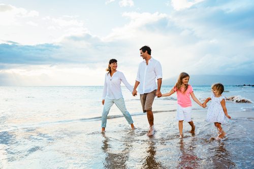 Du siehst eine glückliche und gesund aussehende Familie, Mutter, Vater, 2 Kinder am Strand spazieren gehen.